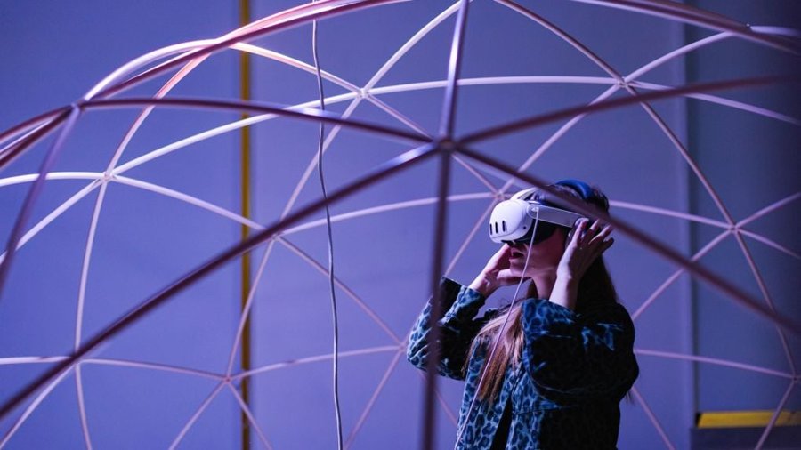 Woman wearing a VR headset inside a geodesic dome structure bathed in purple light