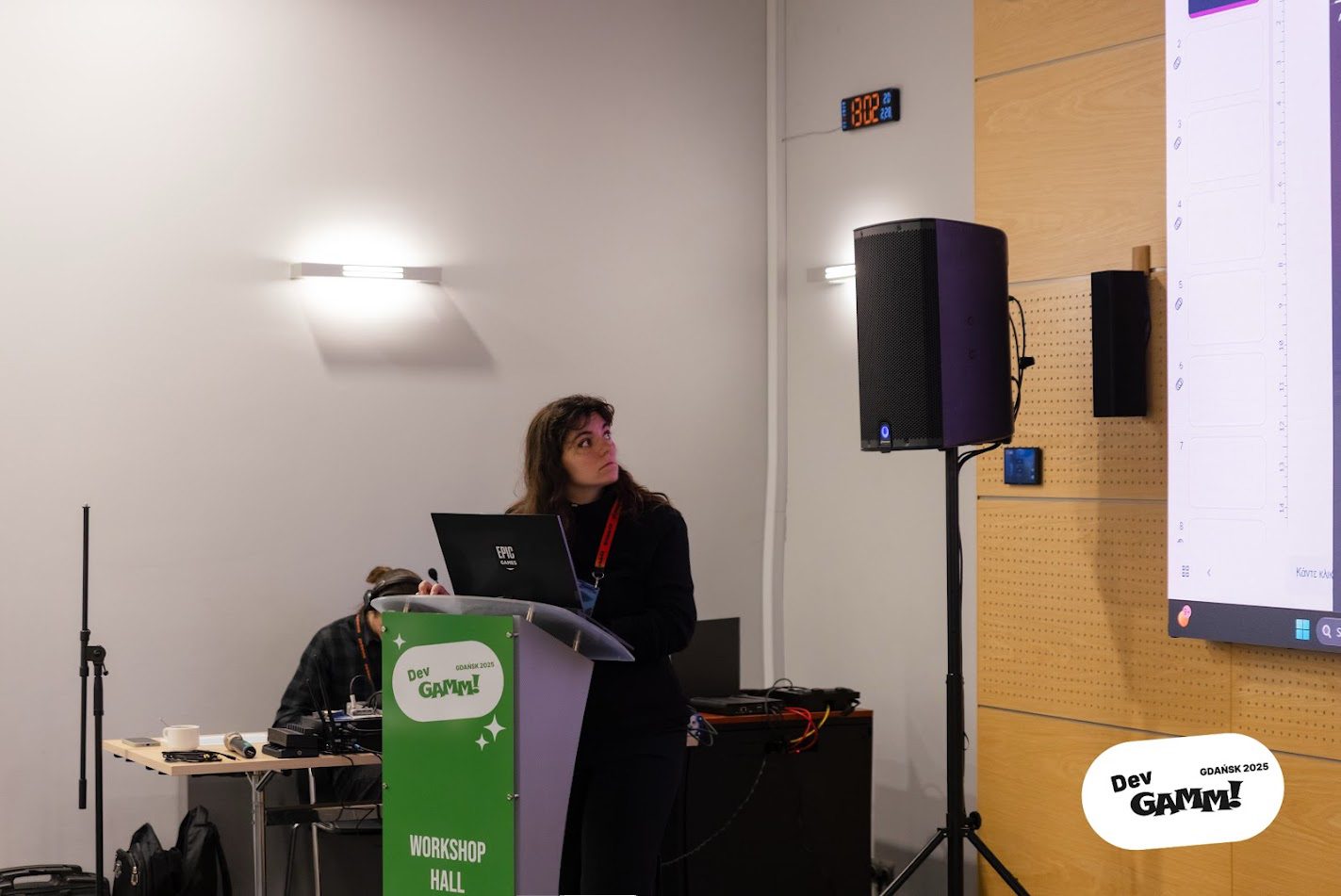 Elena Dimopoulou presenting at the podium in the Workshop Hall at DevGAMM Gdańsk, February 2025